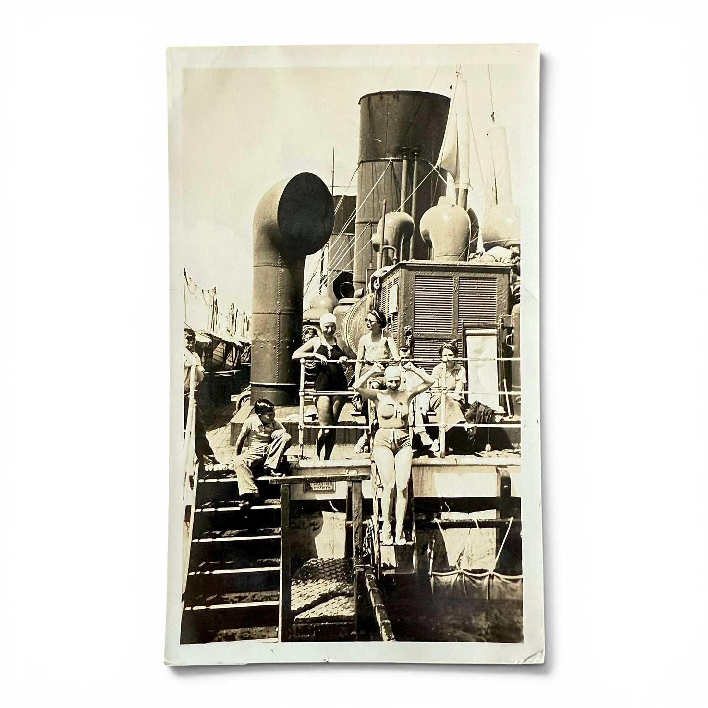 Vintage black and white photograph of people on a ship's deck with visible ship equipment. A woman getting ready to jump into a pool.