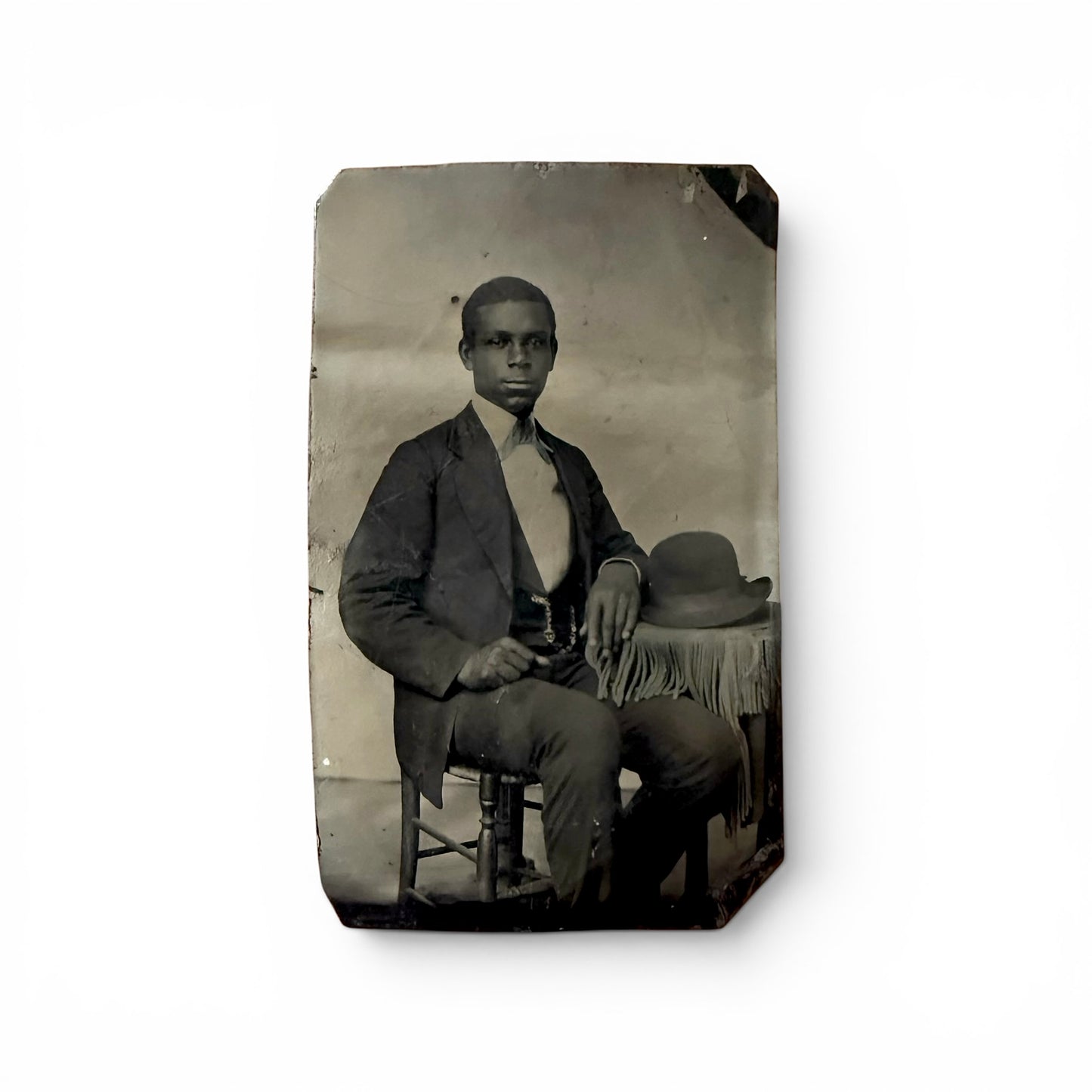 A Man And His Hat - Tintype and african american man sitting for a picture with his arm on a table and a hat sitting on it as well.