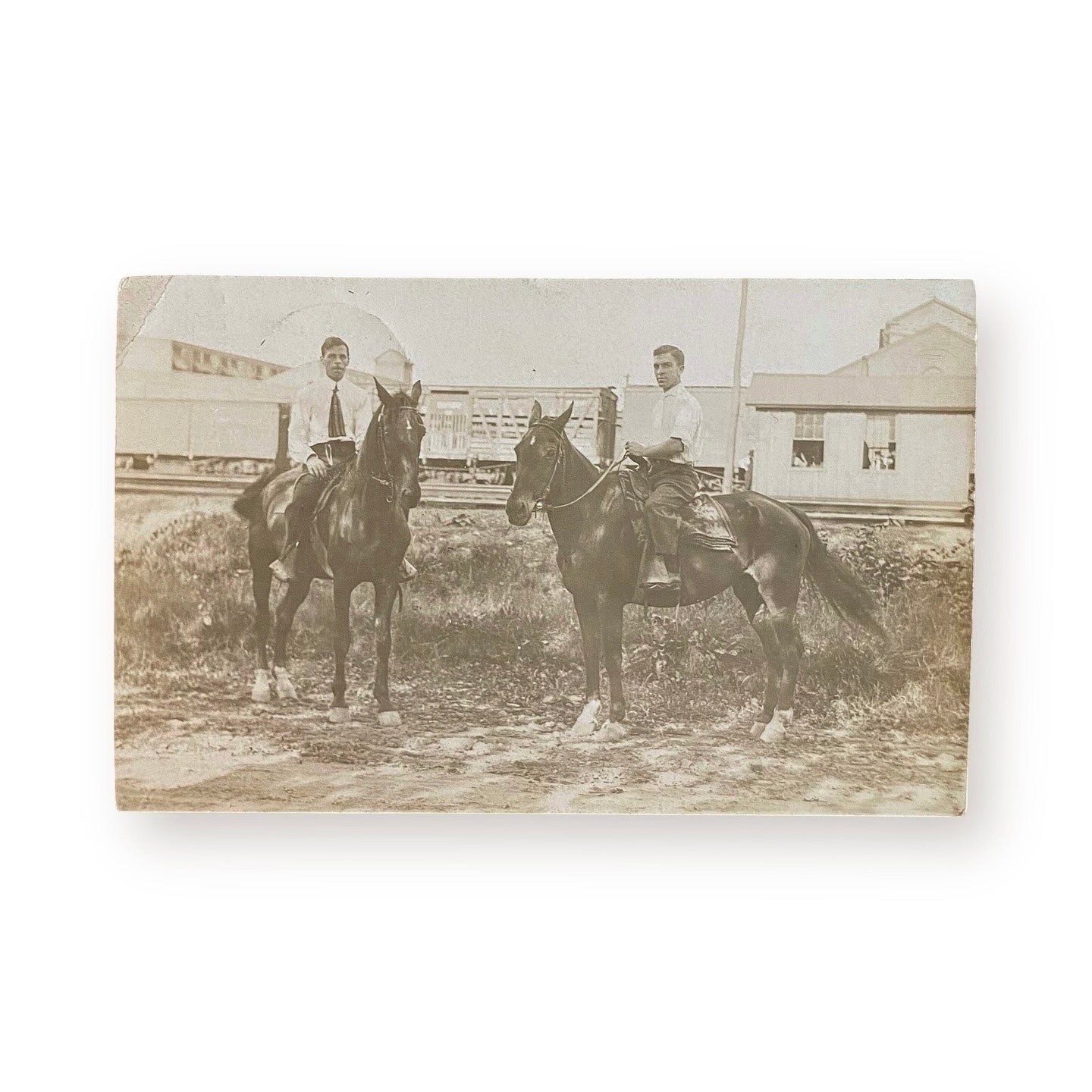 two guys sitting on their own horses outside a train station.