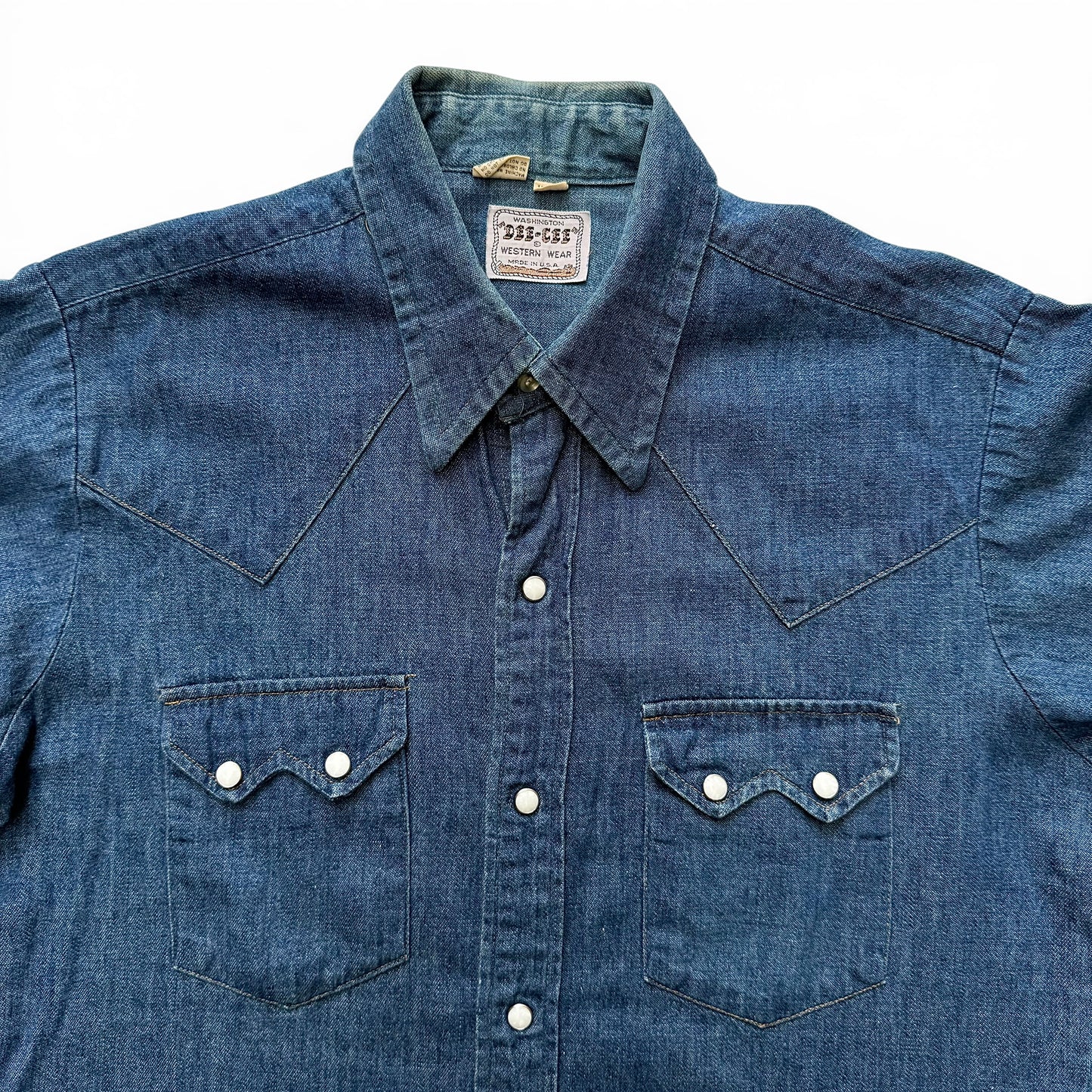 1960s Dee Cee Denim Sawtooth Western Shirt Blue denim shirt with button details on a white background