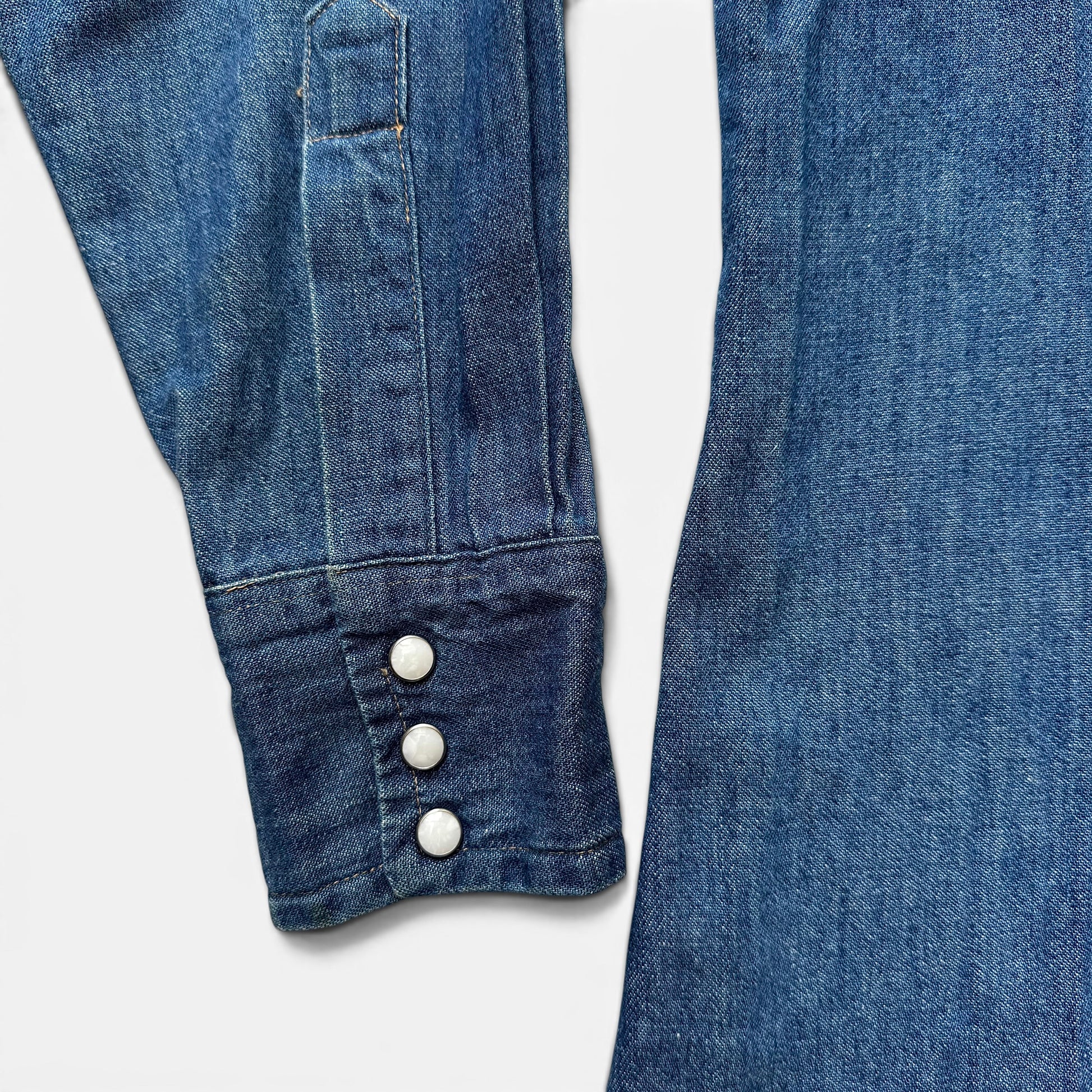 1960s Dee Cee Denim Sawtooth Western Shirt Close-up of blue denim jeans with button details on a white background