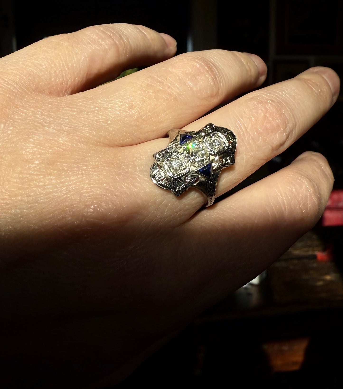 Hand wearing an art deco cocktail engagement ring with diamonds and sapphires on a plain background